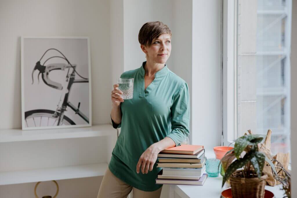 Woman standing by a window holding a glass of water, representing healthy lifestyle factors that may contribute to early menopause.