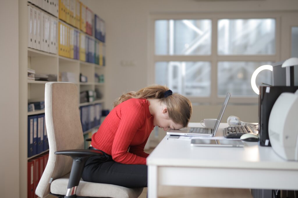 Exhausted office worker asleep at her desk in front of a laptop, illustrating the effects of sleep deprivation and fatigue.