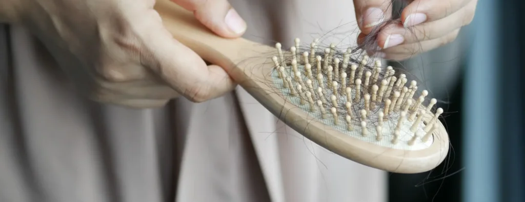 Close-up of a person removing loose strands of hair from a wooden hairbrush, illustrating everyday hair shedding.