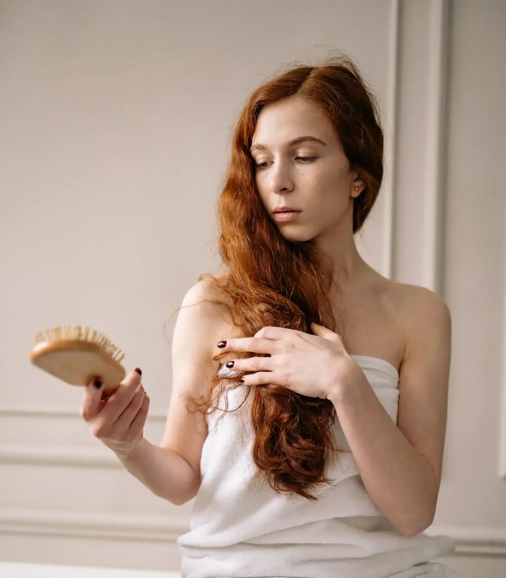 Woman in a towel gently examining long hair with a brush, illustrating concerns about normal hair shedding and hair loss.