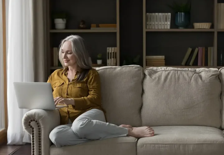 Woman sitting on a couch using a laptop during a telehealth appointment from home.