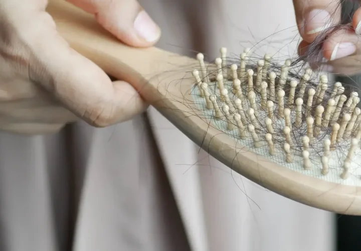 Close-up of a person removing loose strands of hair from a wooden hairbrush, illustrating everyday hair shedding.