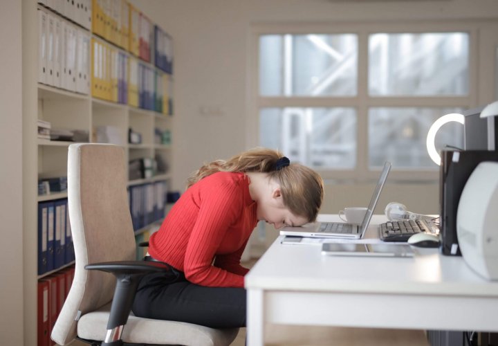 Exhausted office worker asleep at her desk in front of a laptop, illustrating the effects of sleep deprivation and fatigue.